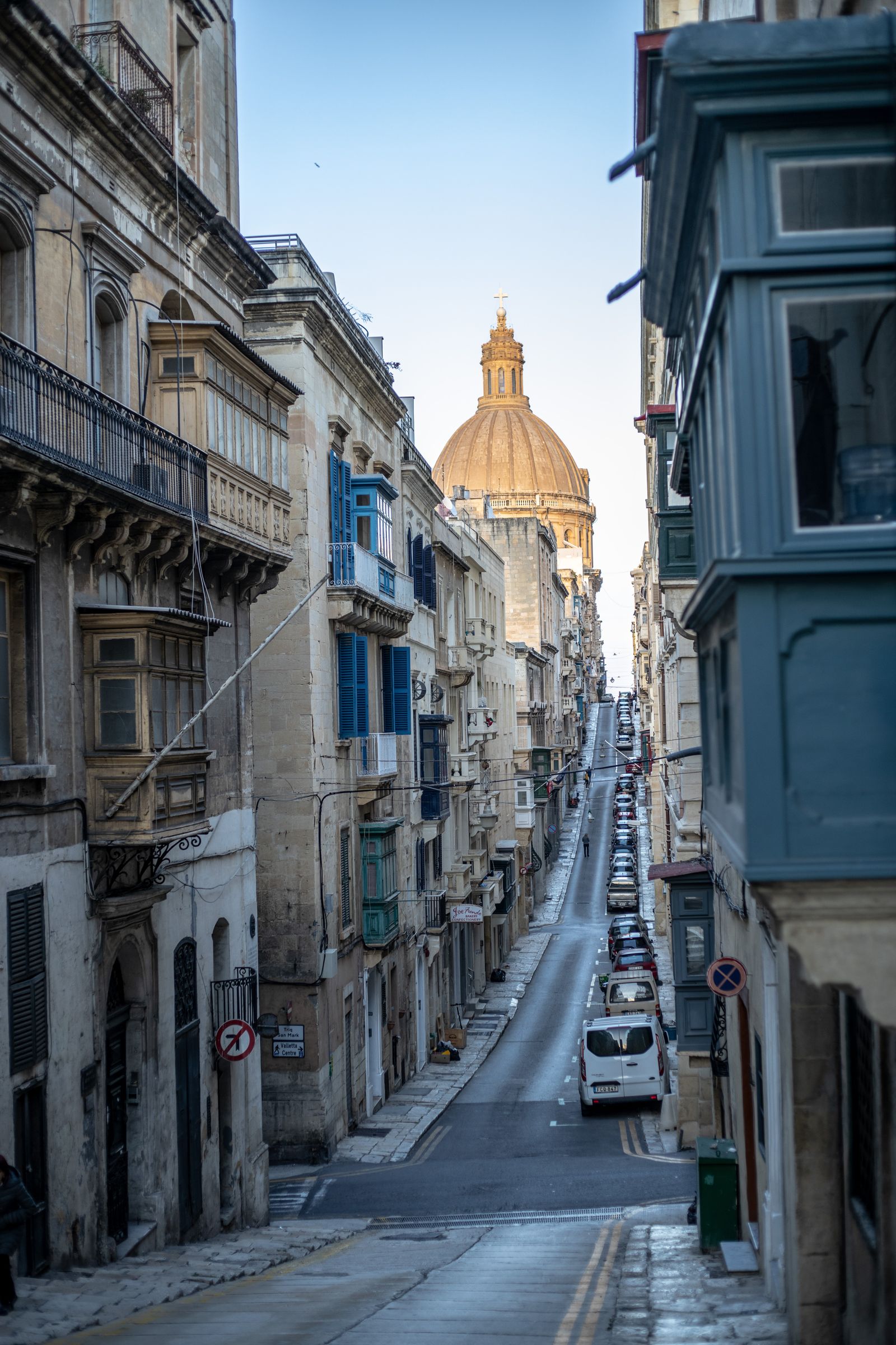 A narrow Maltese street with a church dome rising above the rooftops